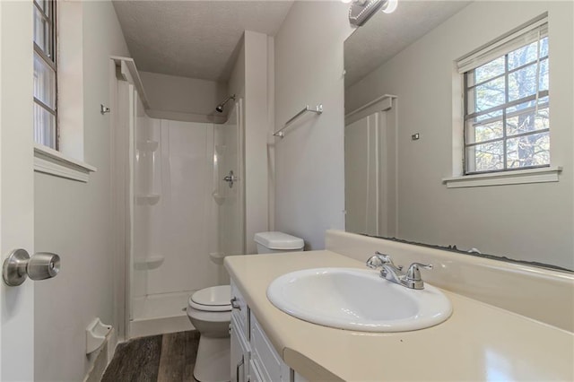 bathroom featuring vanity, wood-type flooring, a textured ceiling, a shower, and toilet