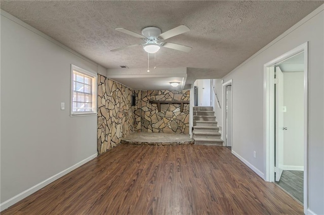 basement with ceiling fan, a stone fireplace, dark hardwood / wood-style floors, and a textured ceiling