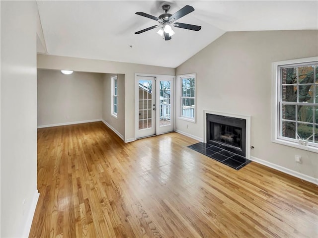 unfurnished living room with a tiled fireplace, ceiling fan, vaulted ceiling, and light wood-type flooring