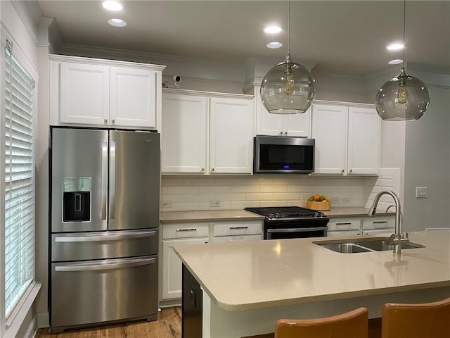 kitchen with sink, a center island with sink, hanging light fixtures, stainless steel appliances, and white cabinets