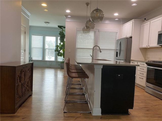 kitchen with a kitchen breakfast bar, decorative light fixtures, stainless steel appliances, white cabinets, and a kitchen island with sink