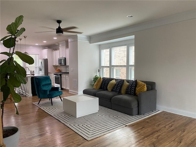 living room with light hardwood / wood-style floors, ceiling fan, and ornamental molding