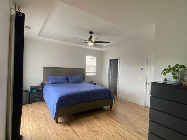 bedroom with a tray ceiling, ceiling fan, and light wood-type flooring