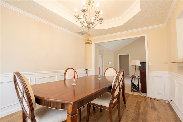dining area featuring a chandelier, light wood-style floors, a wainscoted wall, a decorative wall, and ornamental molding