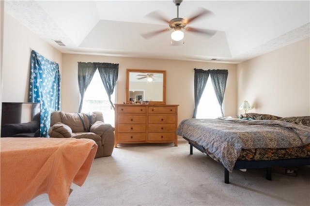 bedroom with a raised ceiling, light carpet, and a ceiling fan