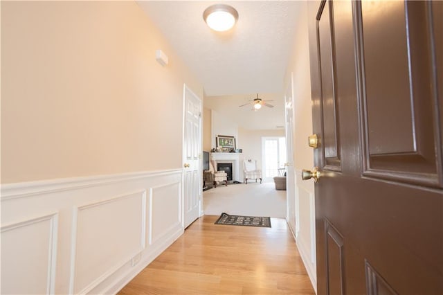 hall with light wood-style flooring, wainscoting, a decorative wall, and a textured ceiling