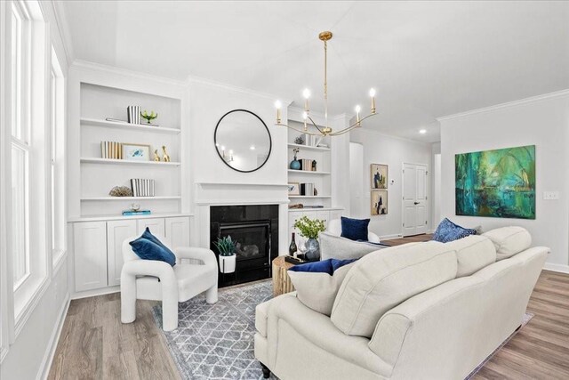 living room featuring crown molding, a notable chandelier, light wood-type flooring, and built in shelves