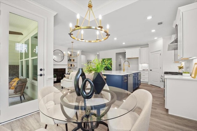 dining area with ornamental molding, sink, a notable chandelier, and light hardwood / wood-style flooring