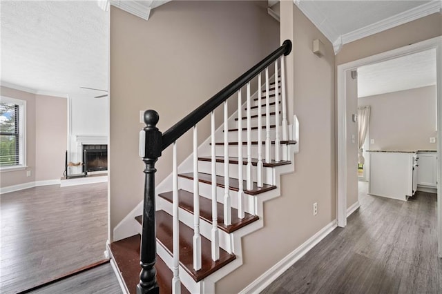 stairway with baseboards, ornamental molding, a fireplace, and wood finished floors