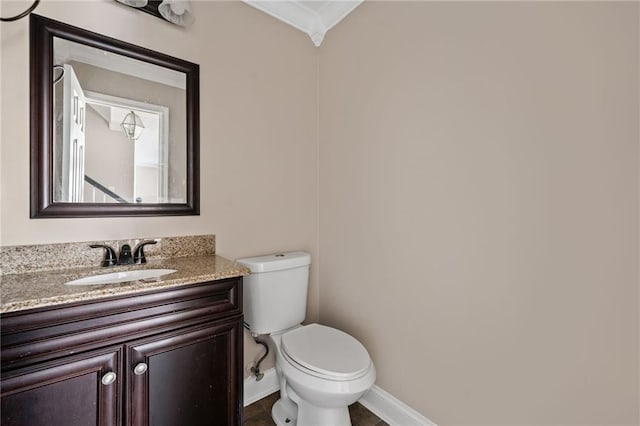 half bathroom with vanity, baseboards, ornamental molding, and toilet
