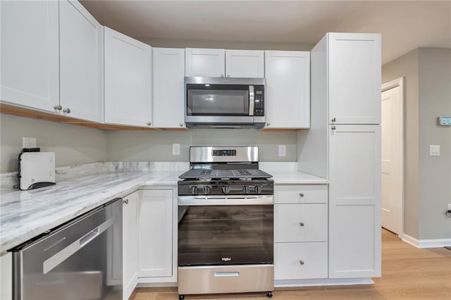 kitchen with light stone counters, light hardwood / wood-style flooring, white cabinets, and appliances with stainless steel finishes