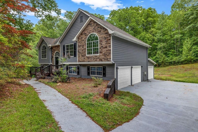 raised ranch featuring an attached garage, a front yard, stone siding, and concrete driveway