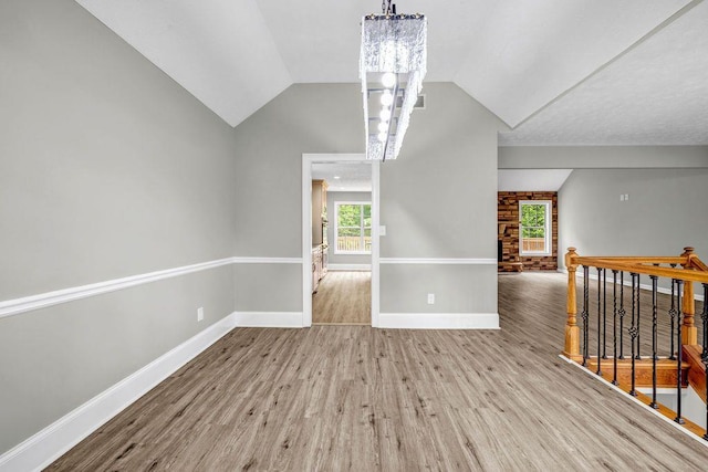 empty room featuring an inviting chandelier, baseboards, vaulted ceiling, and wood finished floors
