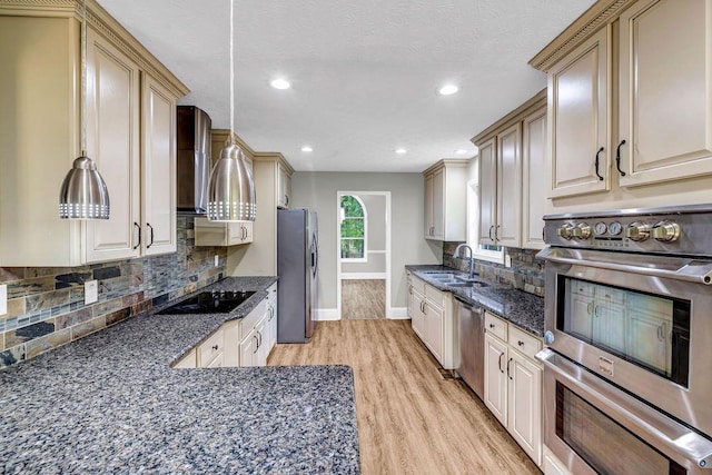 kitchen featuring appliances with stainless steel finishes, a sink, light wood-style floors, baseboards, and tasteful backsplash