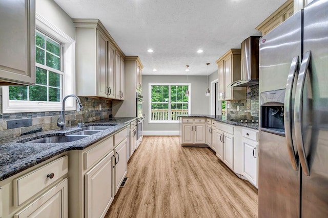 kitchen featuring wall chimney range hood, tasteful backsplash, a sink, light wood-style flooring, and stainless steel appliances