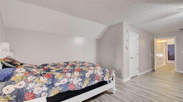 bedroom with a textured ceiling, light hardwood / wood-style floors, and vaulted ceiling