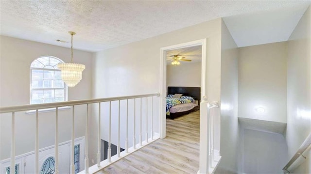 corridor with a notable chandelier, light hardwood / wood-style floors, and a textured ceiling