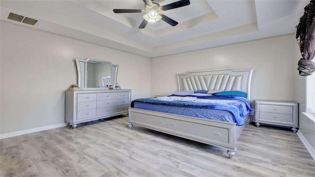 bedroom with light hardwood / wood-style floors, a raised ceiling, and ceiling fan