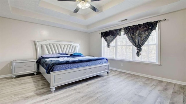 bedroom with ceiling fan, light hardwood / wood-style floors, and a raised ceiling