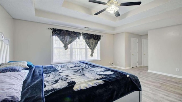 bedroom featuring hardwood / wood-style floors, a raised ceiling, and ceiling fan