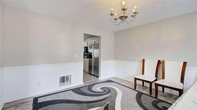 living area with a textured ceiling, light wood-type flooring, and a notable chandelier