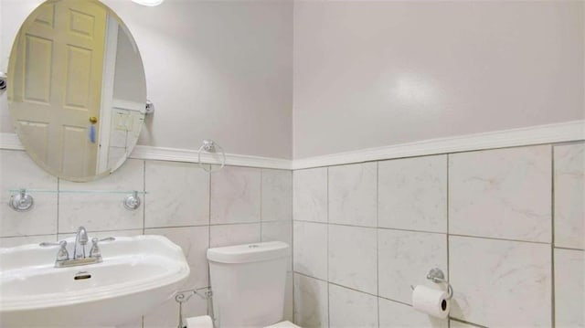 bathroom featuring toilet, tile walls, and sink