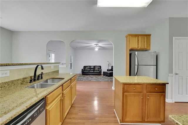 kitchen featuring light stone countertops, arched walkways, a sink, light wood-style flooring, and stainless steel appliances