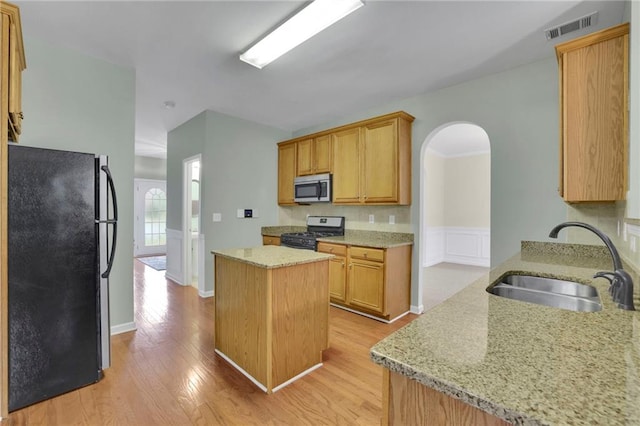 kitchen featuring visible vents, appliances with stainless steel finishes, arched walkways, a sink, and light wood finished floors