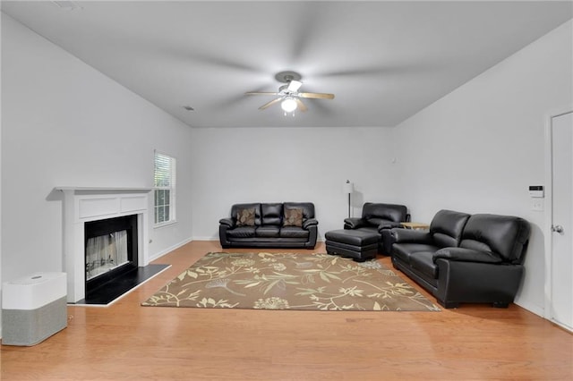 living room with visible vents, a fireplace with raised hearth, ceiling fan, and wood finished floors