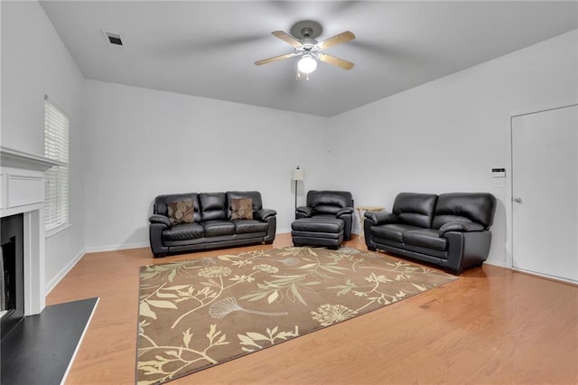 living room featuring a ceiling fan, visible vents, a fireplace, wood finished floors, and baseboards