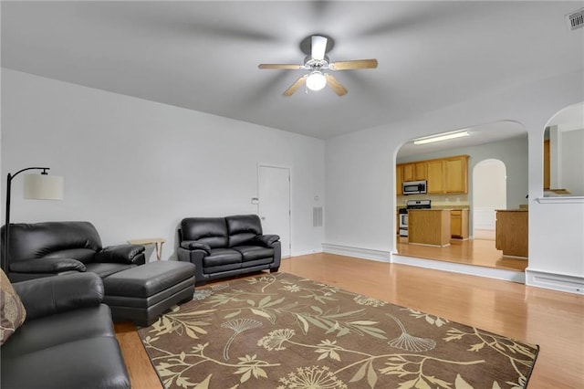 living area with light wood-style floors, arched walkways, ceiling fan, and visible vents