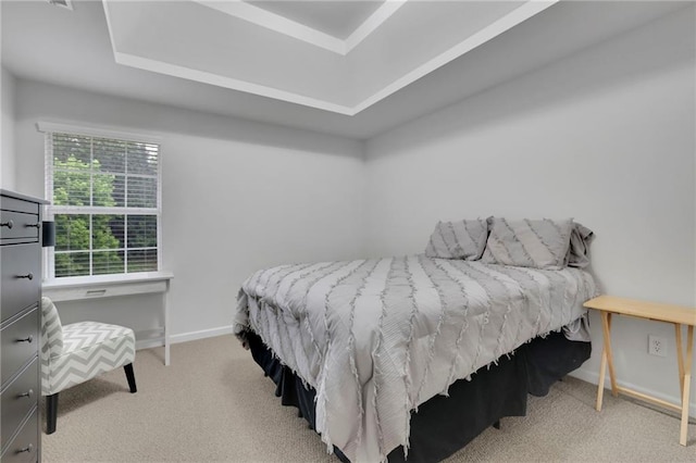 carpeted bedroom with baseboards and a raised ceiling