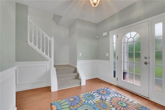 entrance foyer with wood finished floors, a decorative wall, a wainscoted wall, and stairway
