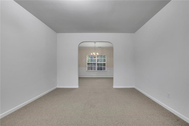 spare room featuring carpet floors, arched walkways, baseboards, and a chandelier