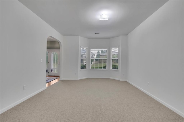 unfurnished room featuring arched walkways, baseboards, and light carpet