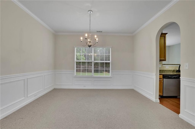 carpeted spare room with ornamental molding, wainscoting, arched walkways, and a notable chandelier