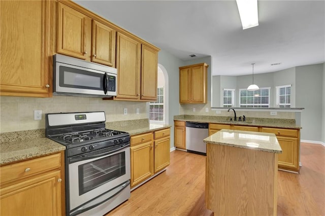 kitchen with a peninsula, appliances with stainless steel finishes, a sink, and light wood-style floors
