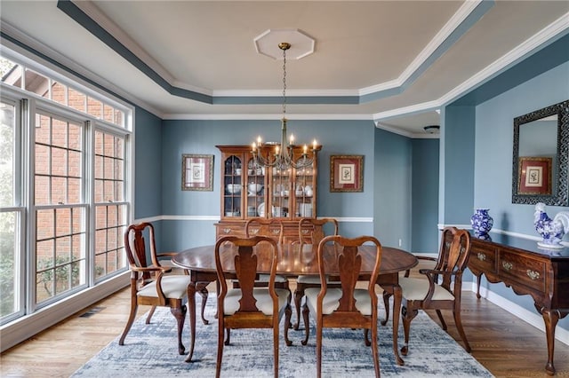 dining room with an inviting chandelier, hardwood / wood-style flooring, crown molding, and a raised ceiling