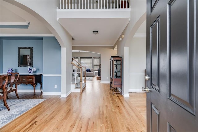 entryway with a towering ceiling, ornamental molding, and light wood-type flooring