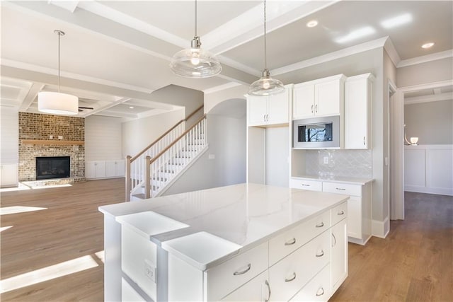 kitchen with pendant lighting, light hardwood / wood-style flooring, stainless steel microwave, light stone counters, and white cabinets