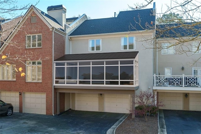 rear view of property featuring stucco siding, driveway, a shingled roof, and a garage