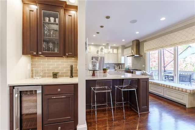 kitchen with dark wood-type flooring, wine cooler, glass insert cabinets, a kitchen breakfast bar, and wall chimney exhaust hood