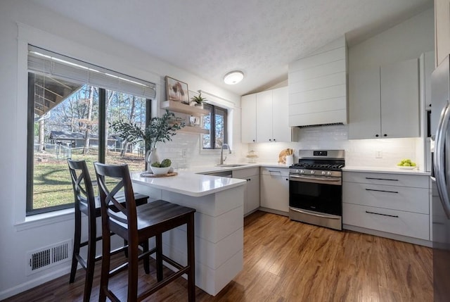 kitchen with visible vents, gas range, a peninsula, vaulted ceiling, and a sink