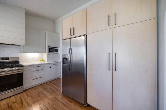 kitchen with light countertops, decorative backsplash, appliances with stainless steel finishes, wall chimney range hood, and light wood-type flooring