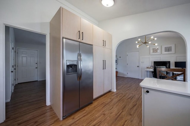 kitchen with arched walkways, a chandelier, wood finished floors, light countertops, and stainless steel fridge