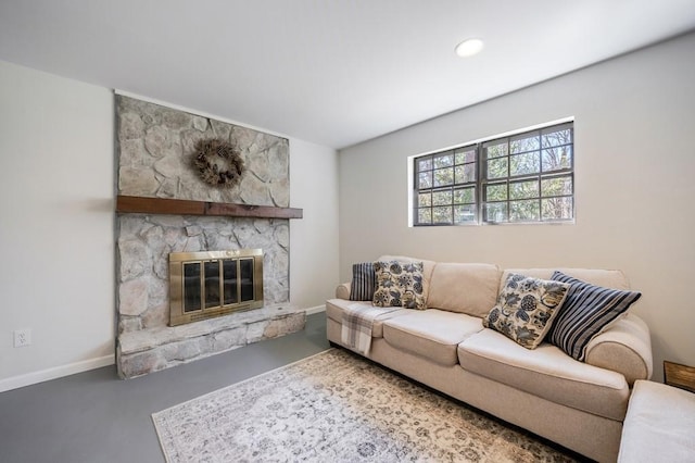 living area with a stone fireplace, baseboards, and finished concrete flooring