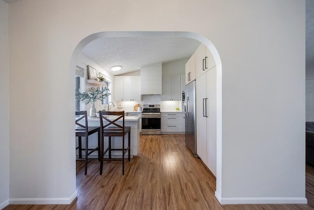 kitchen with tasteful backsplash, arched walkways, stainless steel appliances, light countertops, and light wood-style floors