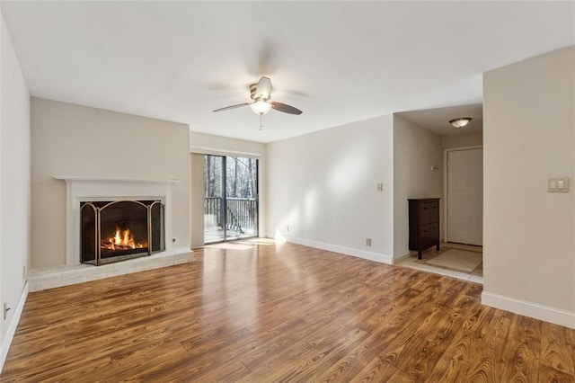 unfurnished living room with a brick fireplace, ceiling fan, baseboards, and wood finished floors