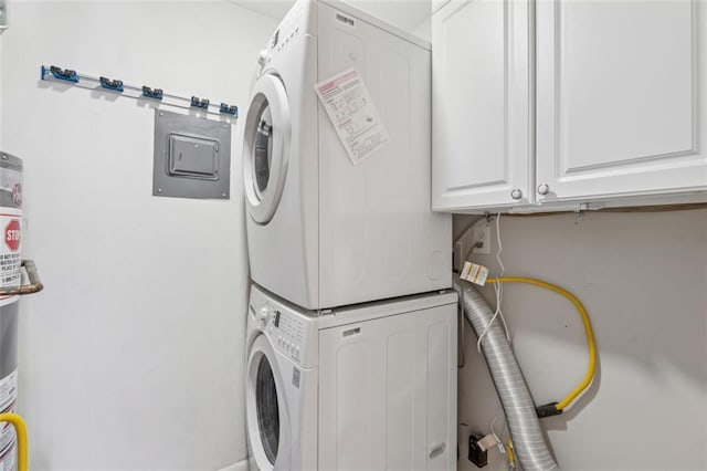 clothes washing area with stacked washer and dryer, electric panel, and cabinet space