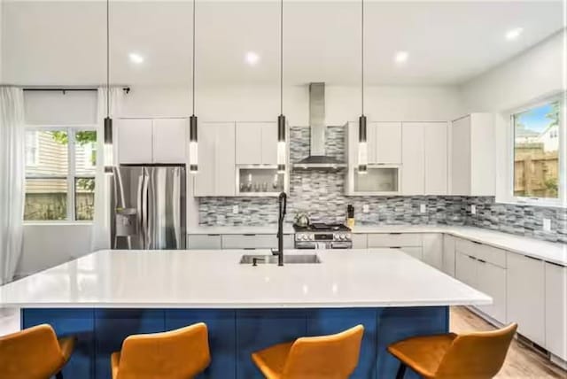 kitchen with a breakfast bar area, a sink, appliances with stainless steel finishes, wall chimney exhaust hood, and modern cabinets